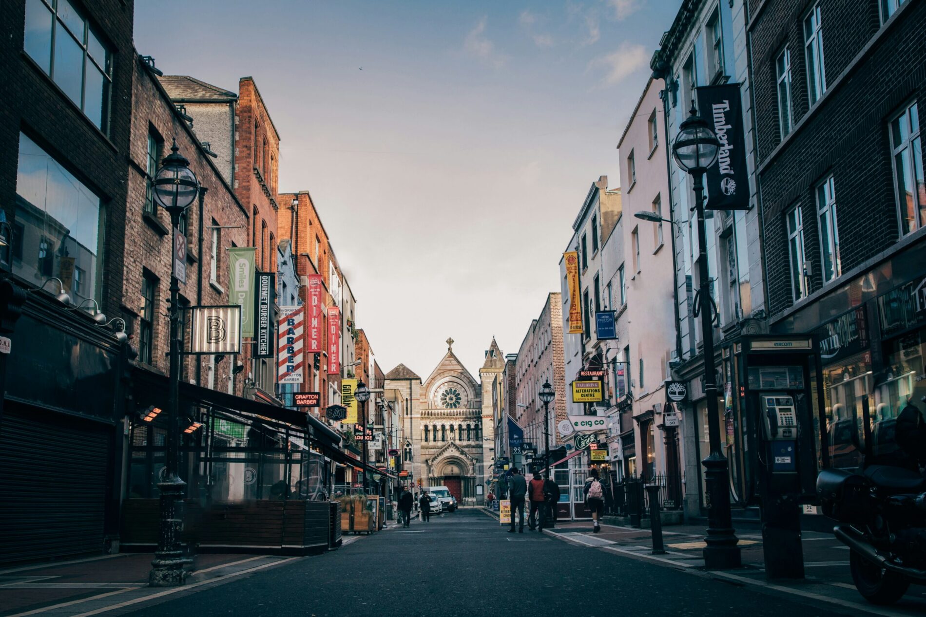Shoppers on a narrow city-centre street lined with terraced buildings at dusk