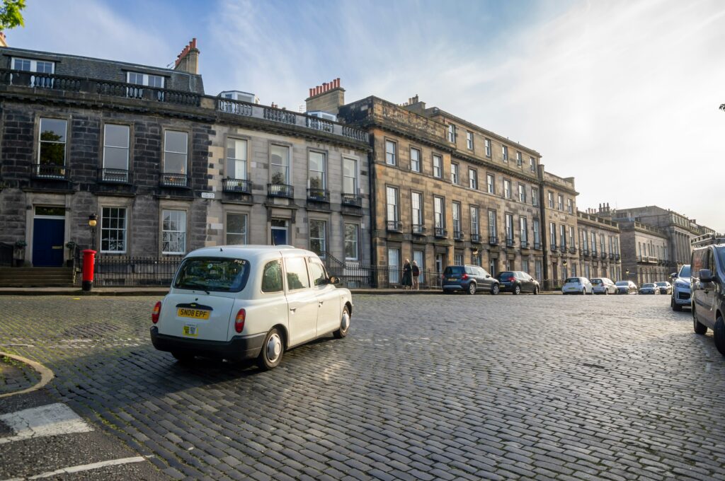 Historic cobblestone street with a white taxi in Edinburgh, Scotland