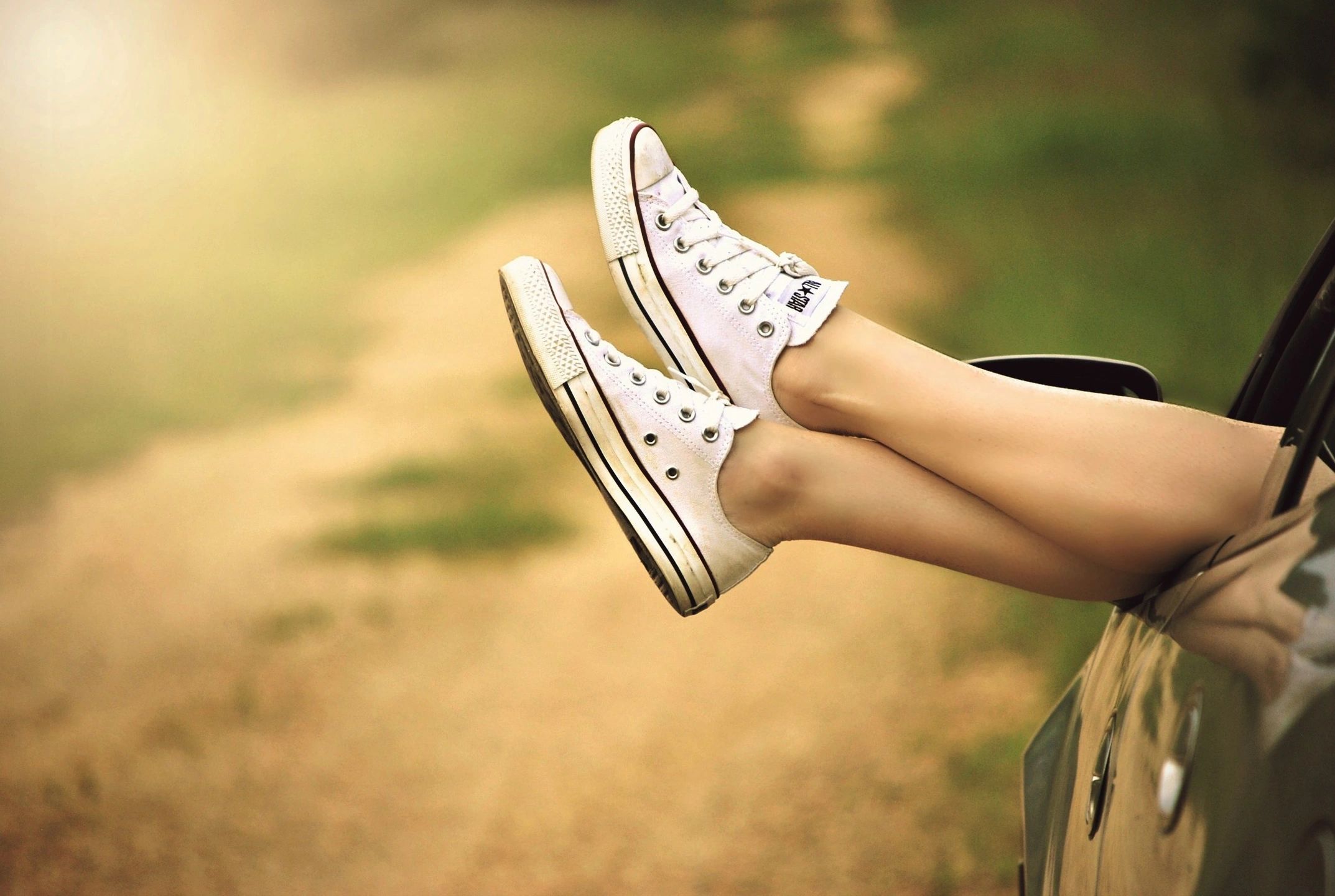 Feet in white sneakers out of an open car window on a sunlit road, the ease behind the best countries for quality of life