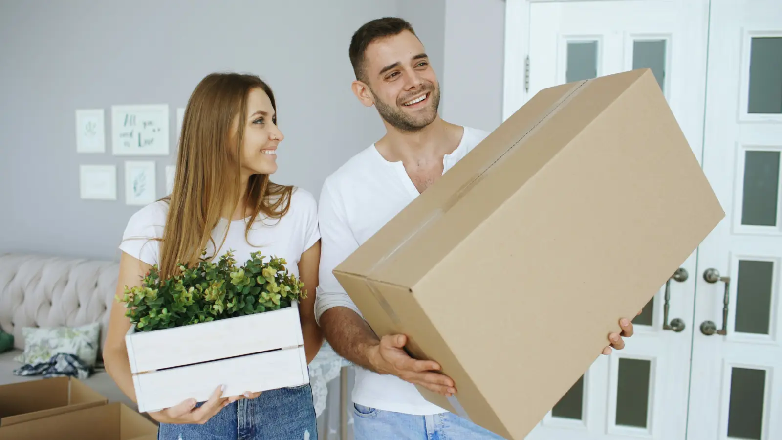 Book international movers ahead of time: couple carrying a moving box and a potted plant